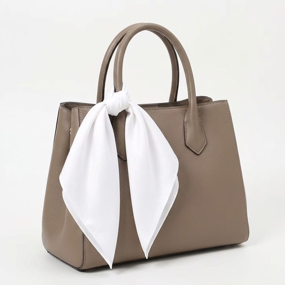Foulard blanc en satin noué sur un sac à main beige, ajoutant une touche élégante et féminine