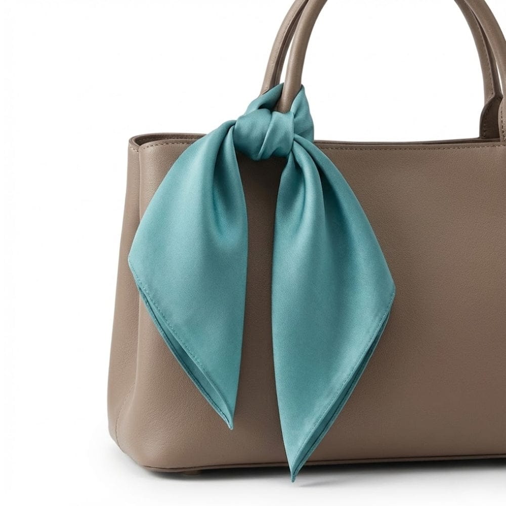 Foulard en soie bleu canard noué sur un sac à main beige, ajoutant une touche élégante à l'ensemble