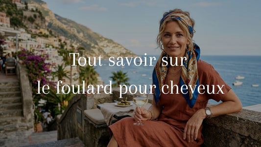 Femme élégante de 50 ans avec un foulard en soie dans les cheveux, posant sur une terrasse ensoleillée face à la mer en Italie.