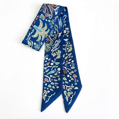 Foulard en satin bleu avec motifs colorés, noué en bandeau sur un fond blanc élégant