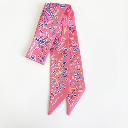 Foulard en satin rose avec motifs colorés, noué en bandeau, idéal comme accessoire chic pour cheveux