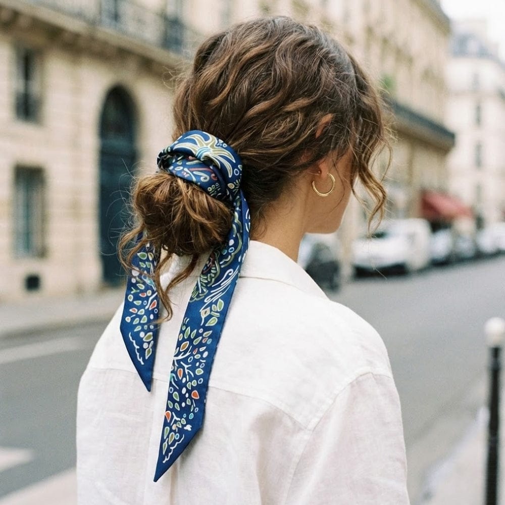 Foulard en satin bleu à motifs floraux noué dans les cheveux d'une femme, en extérieur, avec un décor urbain