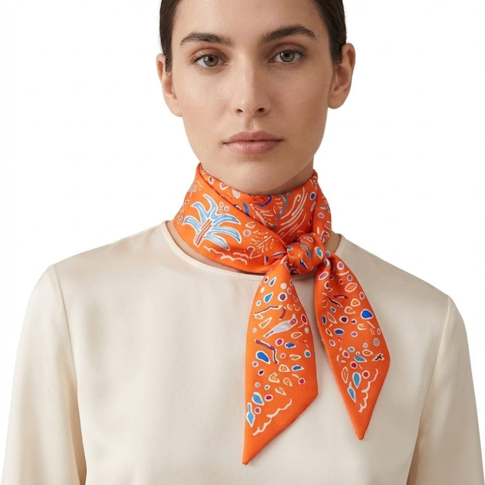 Foulard en satin orange noué autour du cou avec motifs colorés, porté par une femme au teint naturel