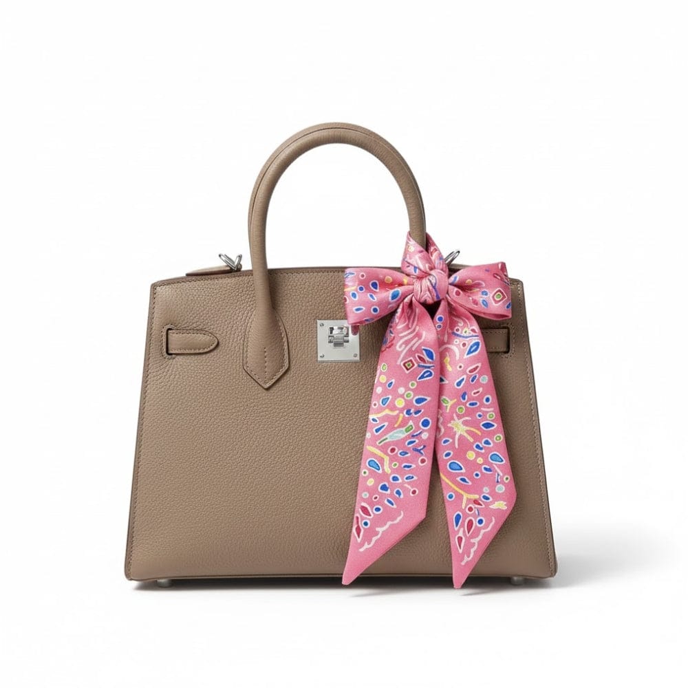 Foulard en satin rose à motifs colorés noué sur un sac à main en cuir beige