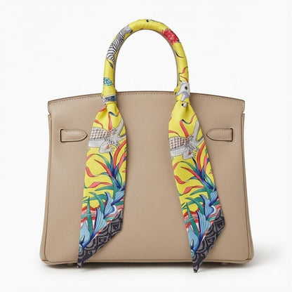 Foulard en soie jaune à motifs colorés noué sur un sac à main beige, ajoutant une touche d'élégance moderne