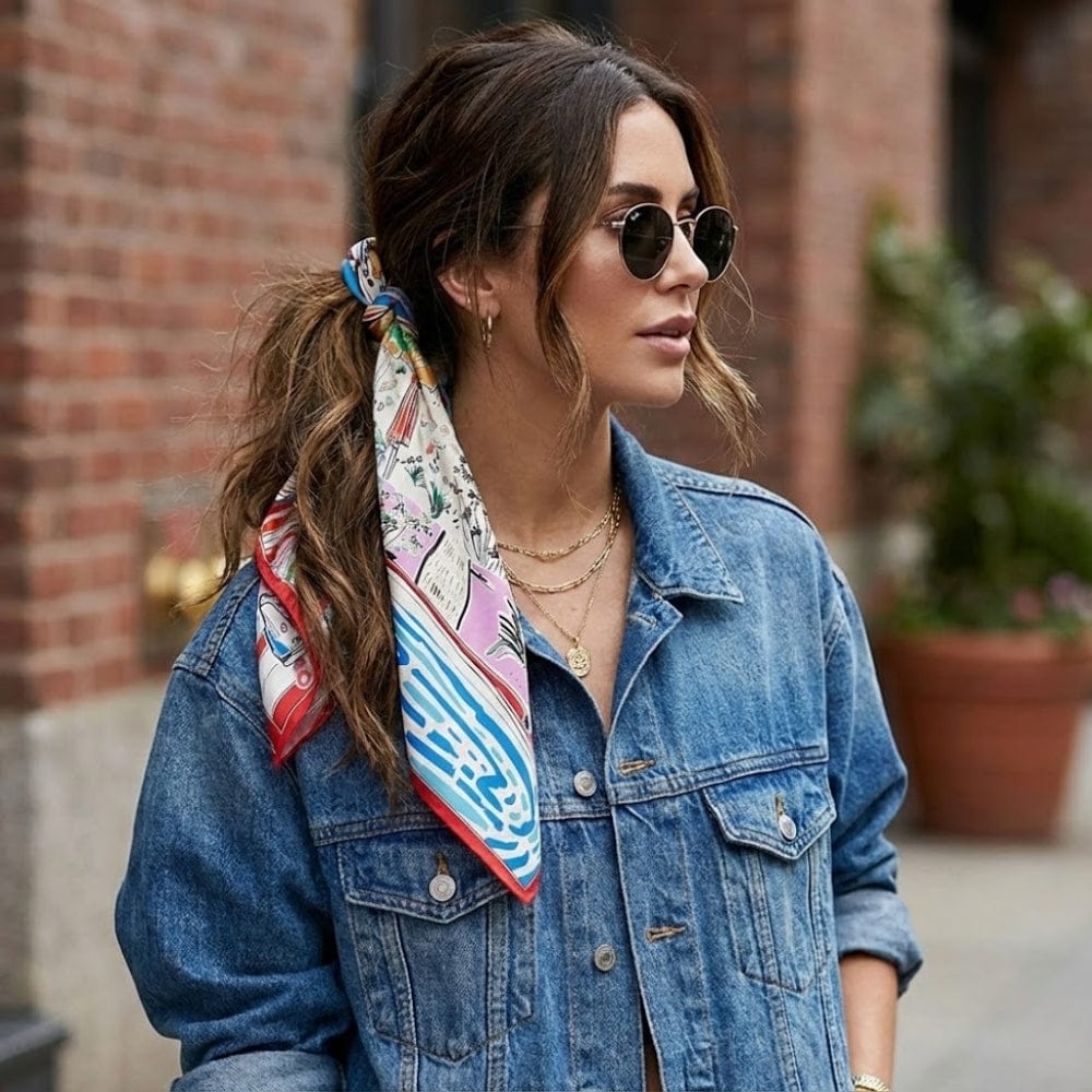Foulard carré en satin aux motifs colorés, noué dans les cheveux d'une femme portant une veste en jean