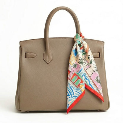 Foulard carré en soie aux motifs colorés, noué sur un sac à main beige pour une touche élégante