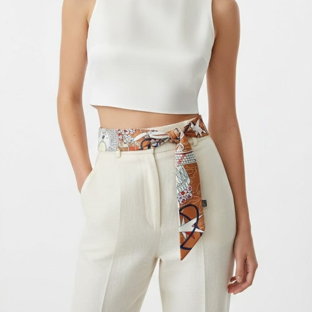Foulard en soie noué à la taille, motifs colorés sur fond marron, porté avec un top blanc et un pantalon