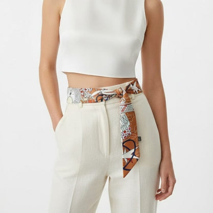Foulard en soie noué à la taille, motifs colorés sur fond marron, porté avec un top blanc et un pantalon