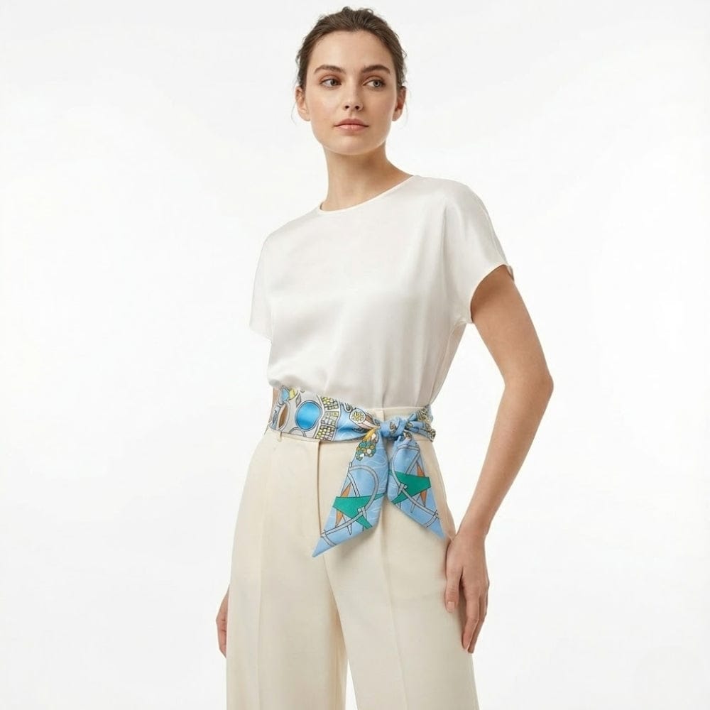 Foulard noué en satin bleu avec motifs géométriques, porté en ceinture par une femme en haut blanc