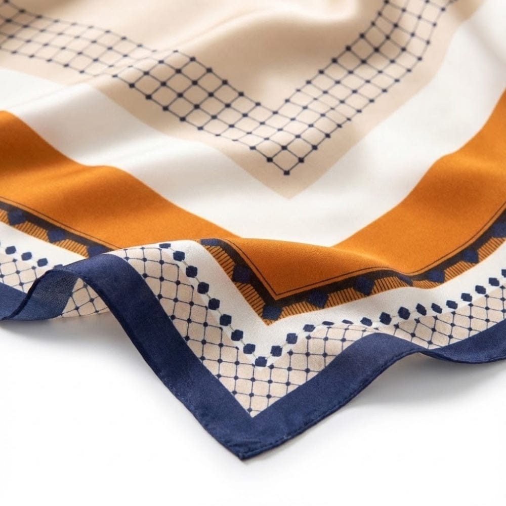 Foulard carré en satin aux motifs géométriques orange, bleu marine et crème, posé sur une surface blanche