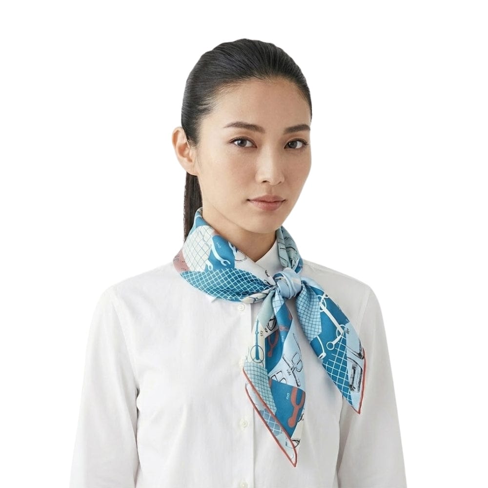 Foulard en soie carré bleu avec motifs graphiques, noué autour du cou d'une femme en chemise blanche
