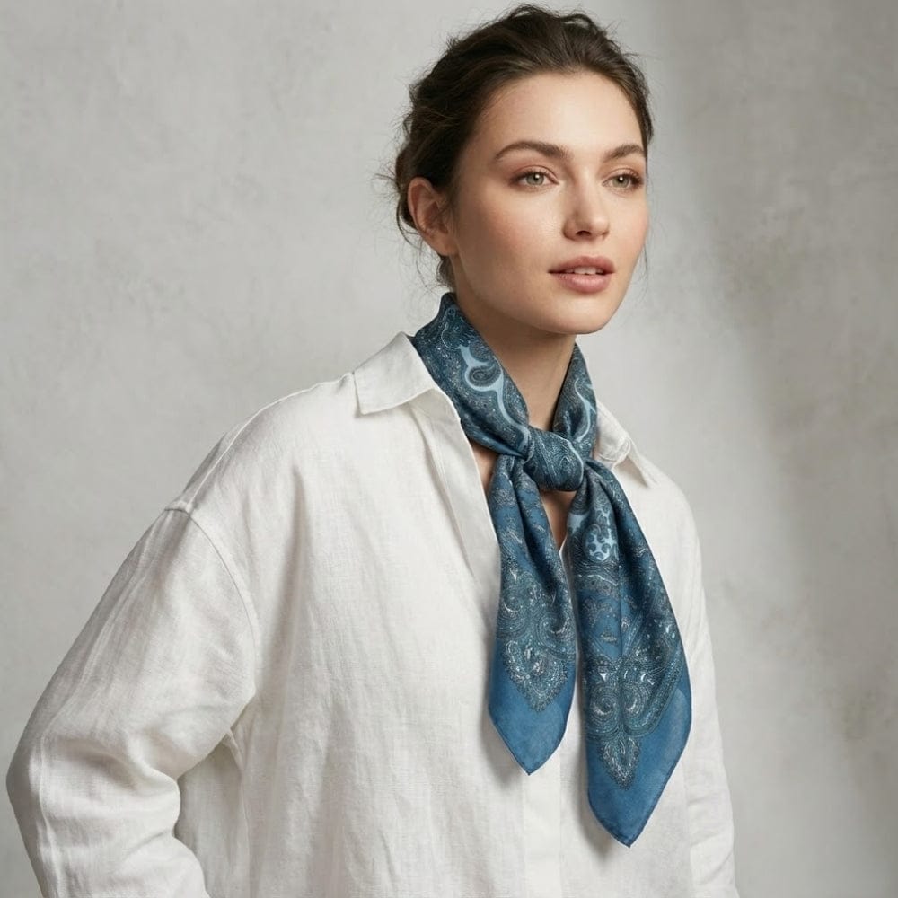 Foulard en satin bleu avec motifs paisley, noué autour du cou d'une femme en chemise blanche