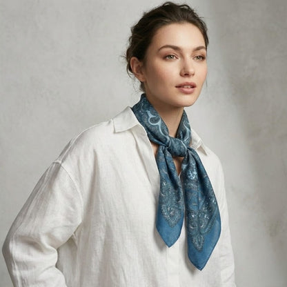 Foulard en satin bleu avec motifs paisley, noué autour du cou d'une femme en chemise blanche