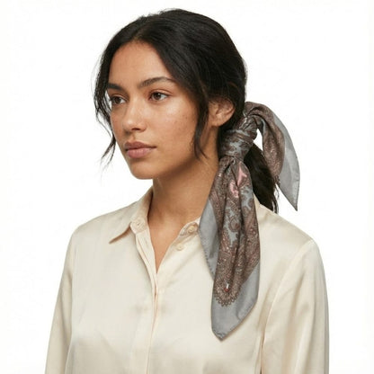 Foulard en satin gris avec motifs floraux, noué sur un chignon, porté par une femme en chemise beige