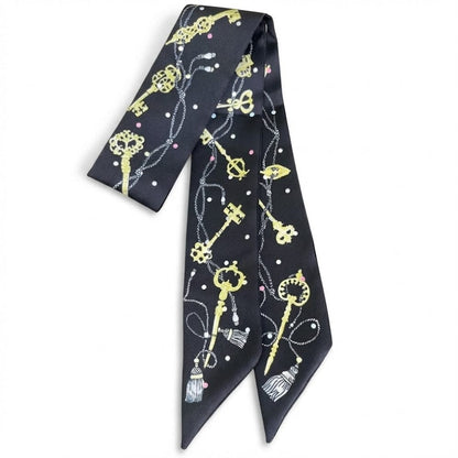 Foulard en satin noir avec motifs de clés dorées et perles colorées, noué élégamment sur une femme
