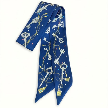 Foulard en satin bleu avec motifs de clés et de perles colorées, noué élégamment sur une femme