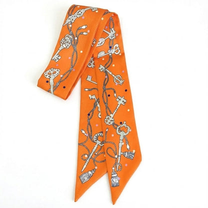 Foulard en satin orange avec motifs de clés et de franges, noué élégamment sur un fond blanc