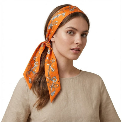Foulard en satin orange noué sur la tête, orné de motifs élégants, porté par une femme dans un décor minimaliste