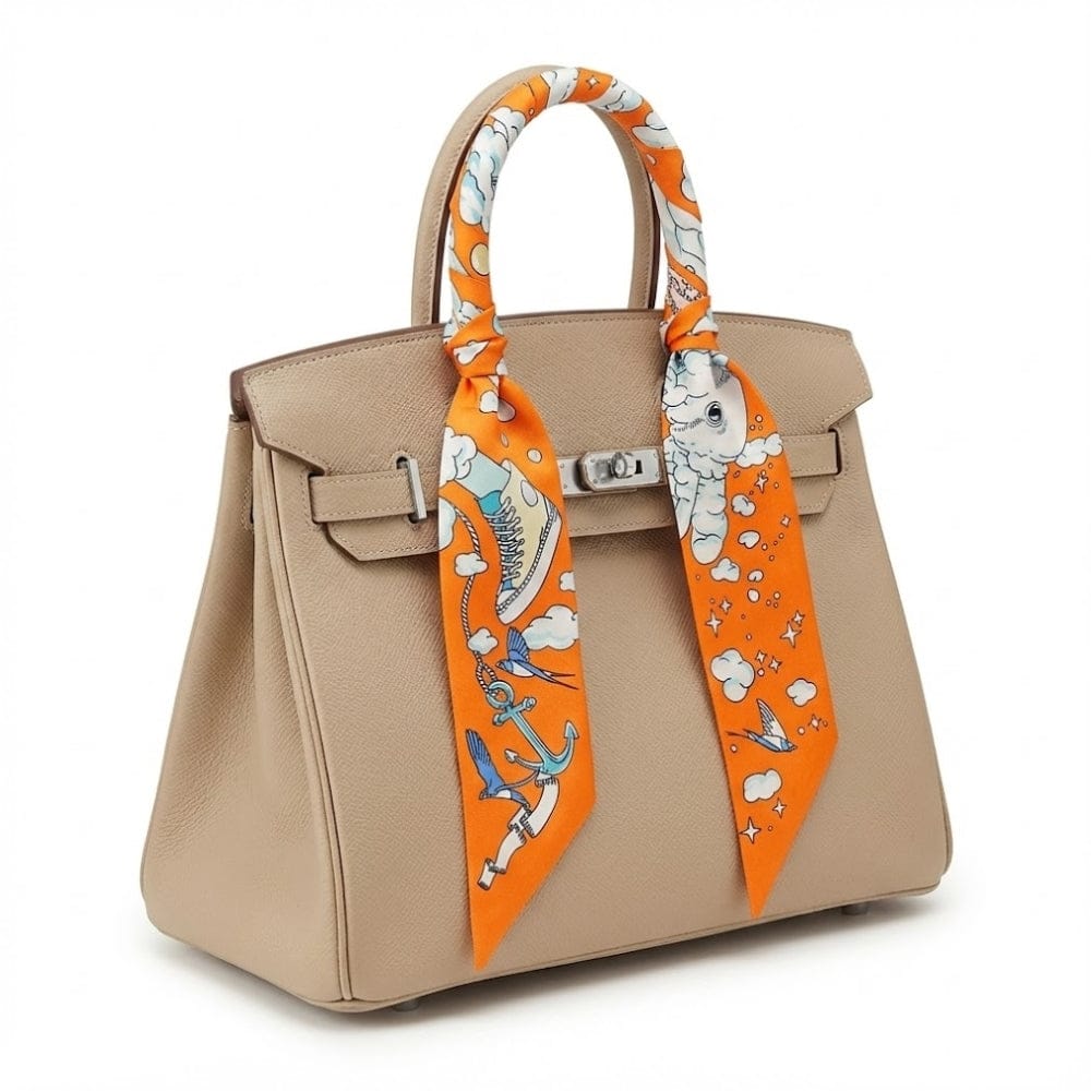Foulard en soie orange à motifs marins noué sur un sac à main beige, ajoutant une touche chic et colorée