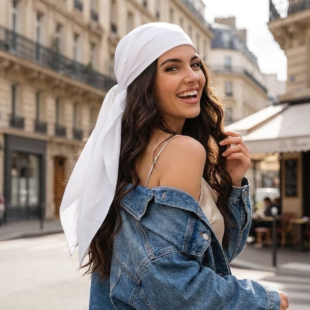 Foulard blanc en satin noué, porté par une femme souriante dans une rue parisienne ensoleillée