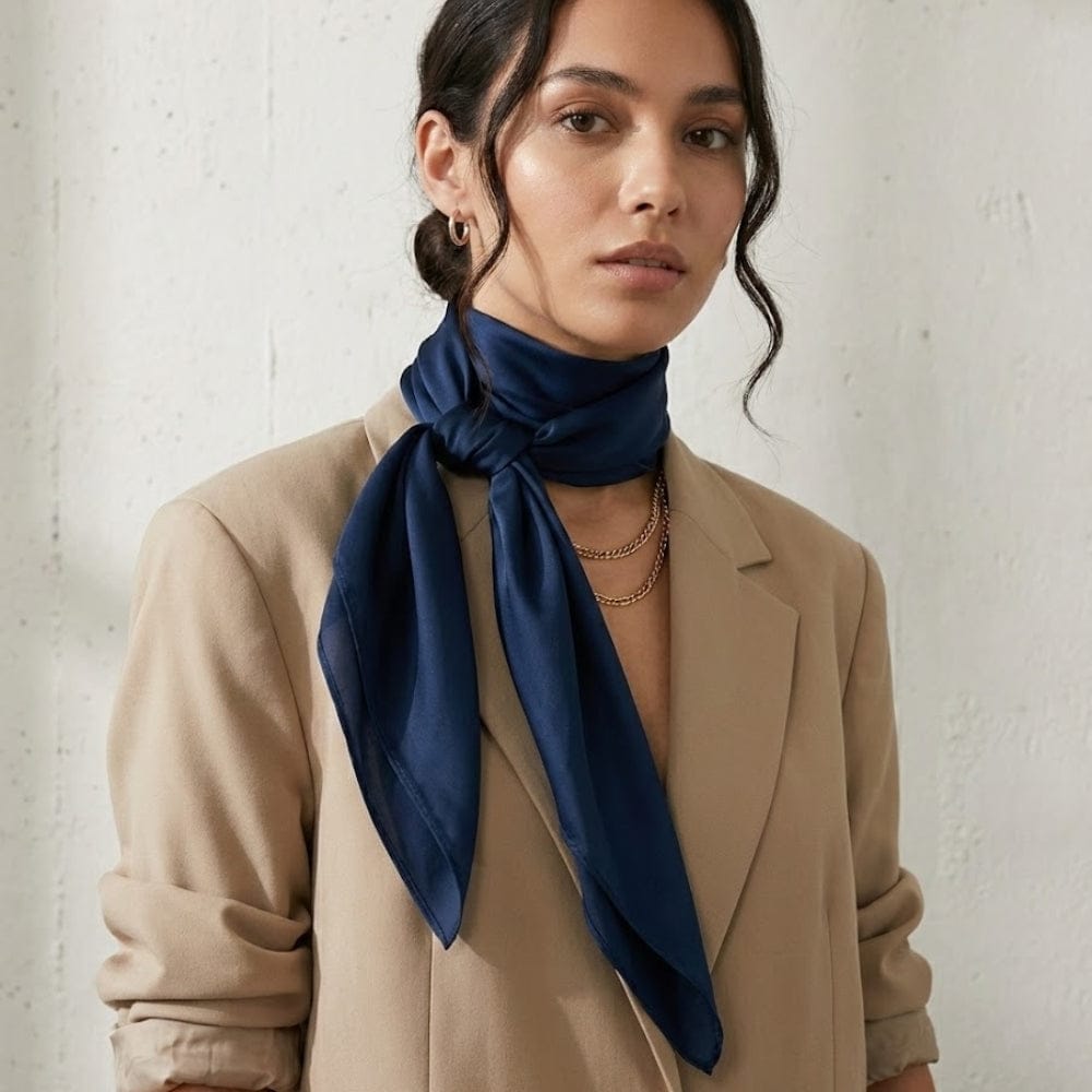 Foulard en satin bleu marine noué élégamment autour du cou d'une femme, porté avec un blazer beige