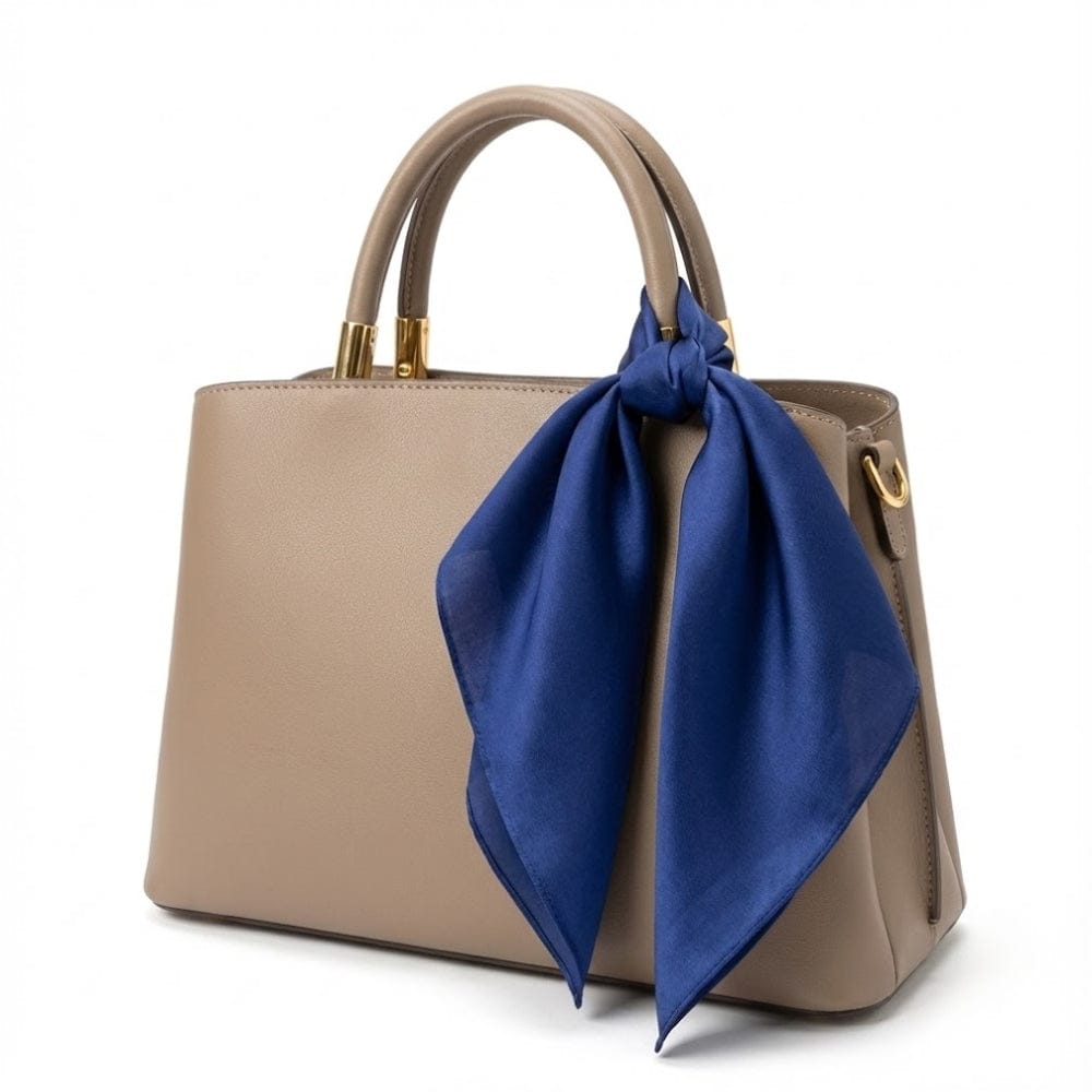 Foulard en soie bleu profond noué sur un sac à main beige, ajoutant une touche élégante et sophistiquée