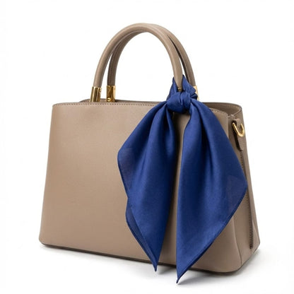 Foulard en soie bleu profond noué sur un sac à main beige, ajoutant une touche élégante et sophistiquée