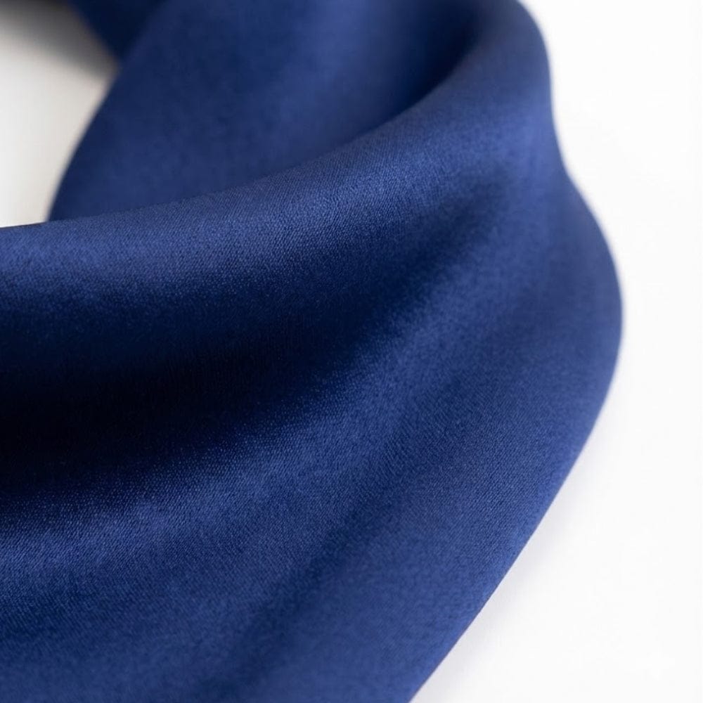 Foulard en soie bleu profond, d'une texture lisse et élégante, drapé avec sophistication sur un fond neutre