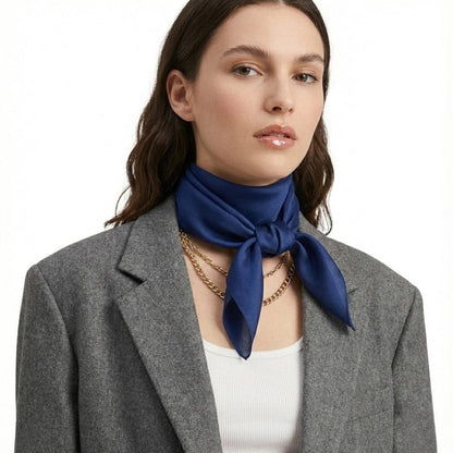 Foulard en soie bleu profond noué autour du cou d'une femme portant un blazer gris