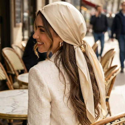 Foulard en satin beige noué sur la tête d'une femme souriante, assise à une terrasse de café chic