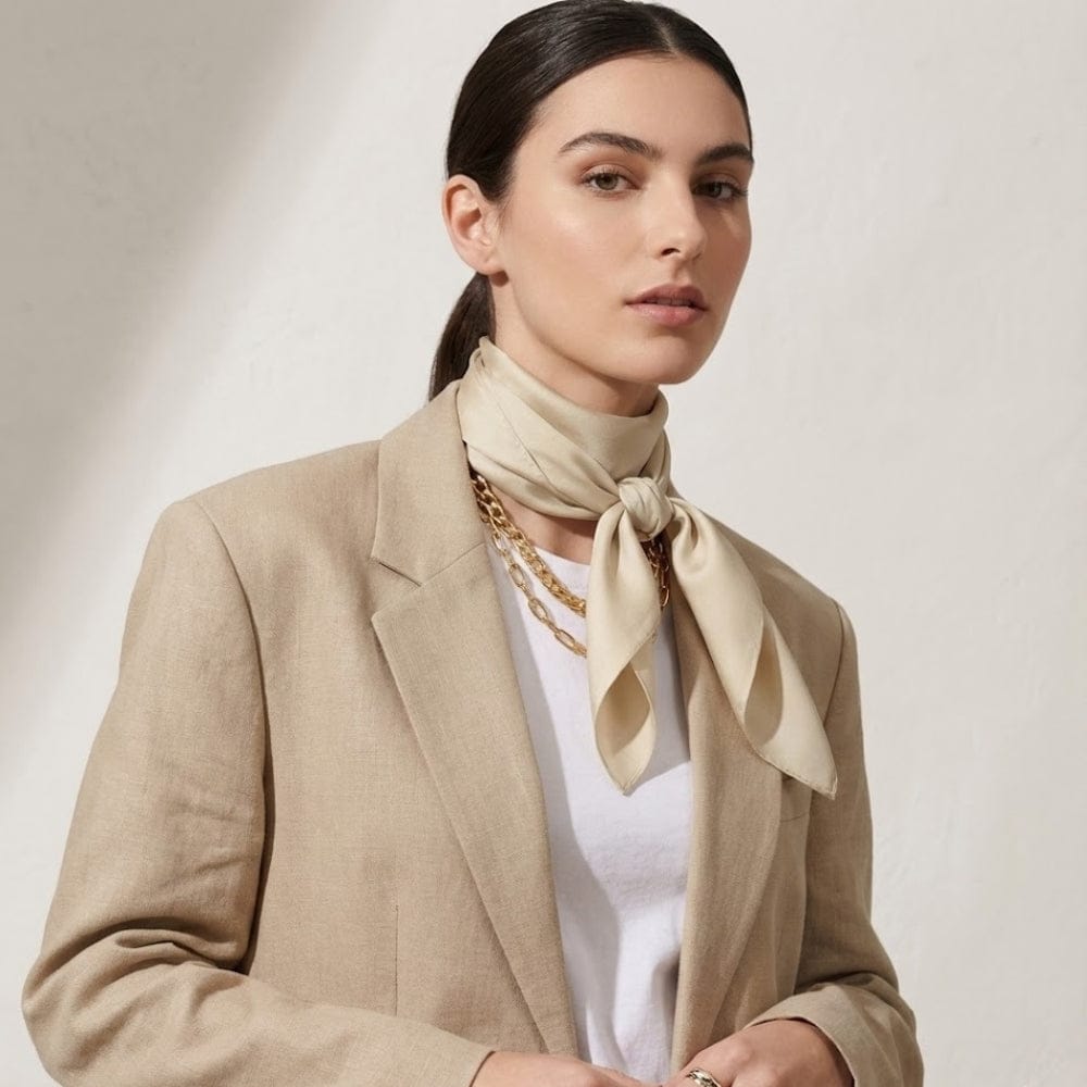 Foulard en satin beige noué autour du cou d'une femme, porté avec un blazer chic sur fond neutre