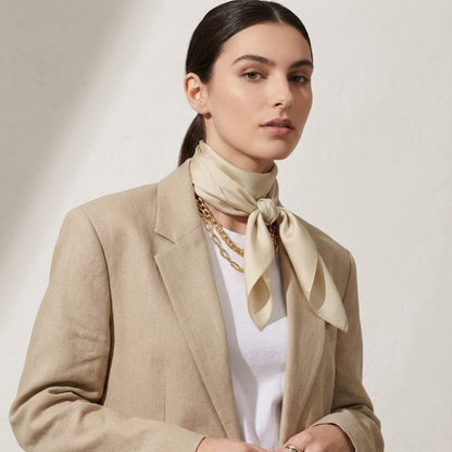 Foulard en satin beige noué autour du cou d'une femme, porté avec un blazer chic sur fond neutre