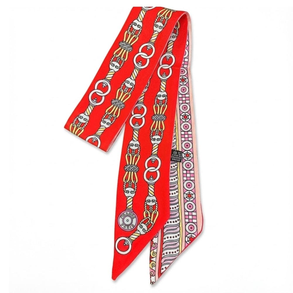 Foulard en soie rouge à motifs géométriques et chaînes, noué élégamment sur une femme
