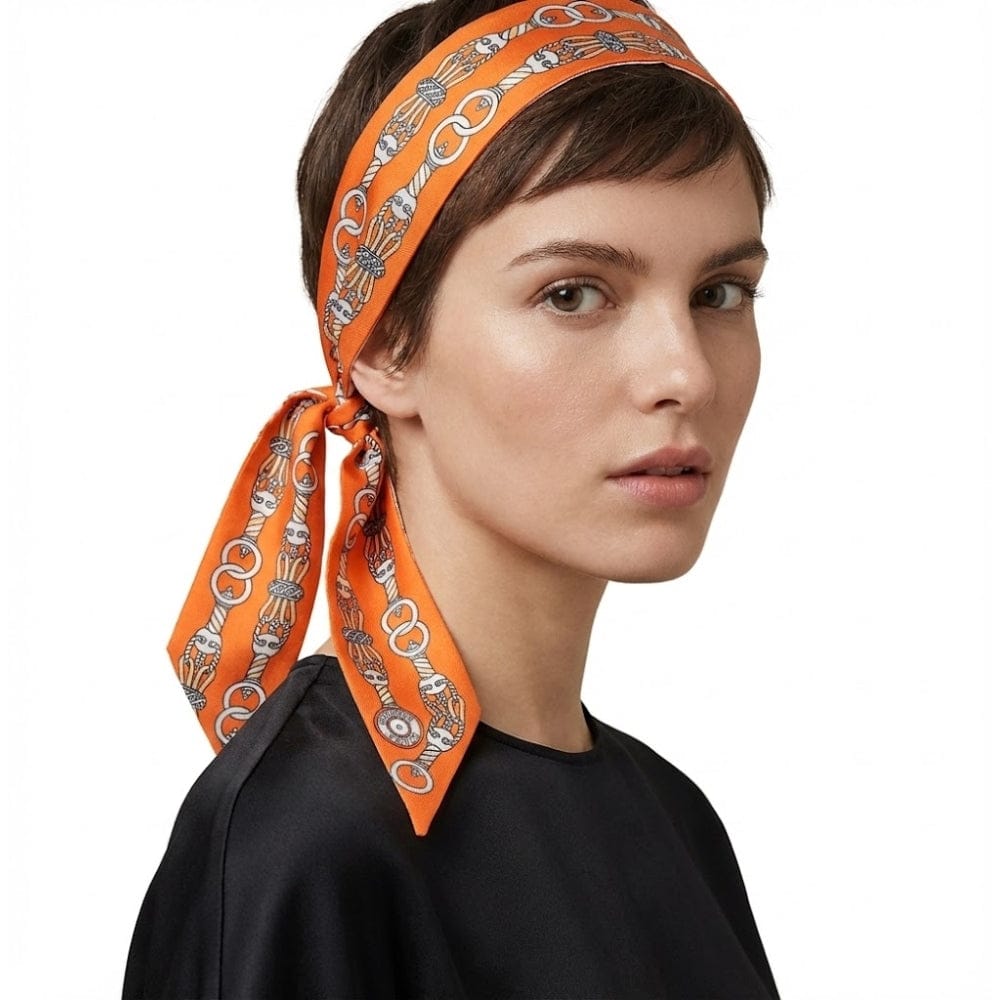 Foulard en satin orange à motifs graphiques, noué sur une coiffure courte, apportant une touche d'élégance moderne