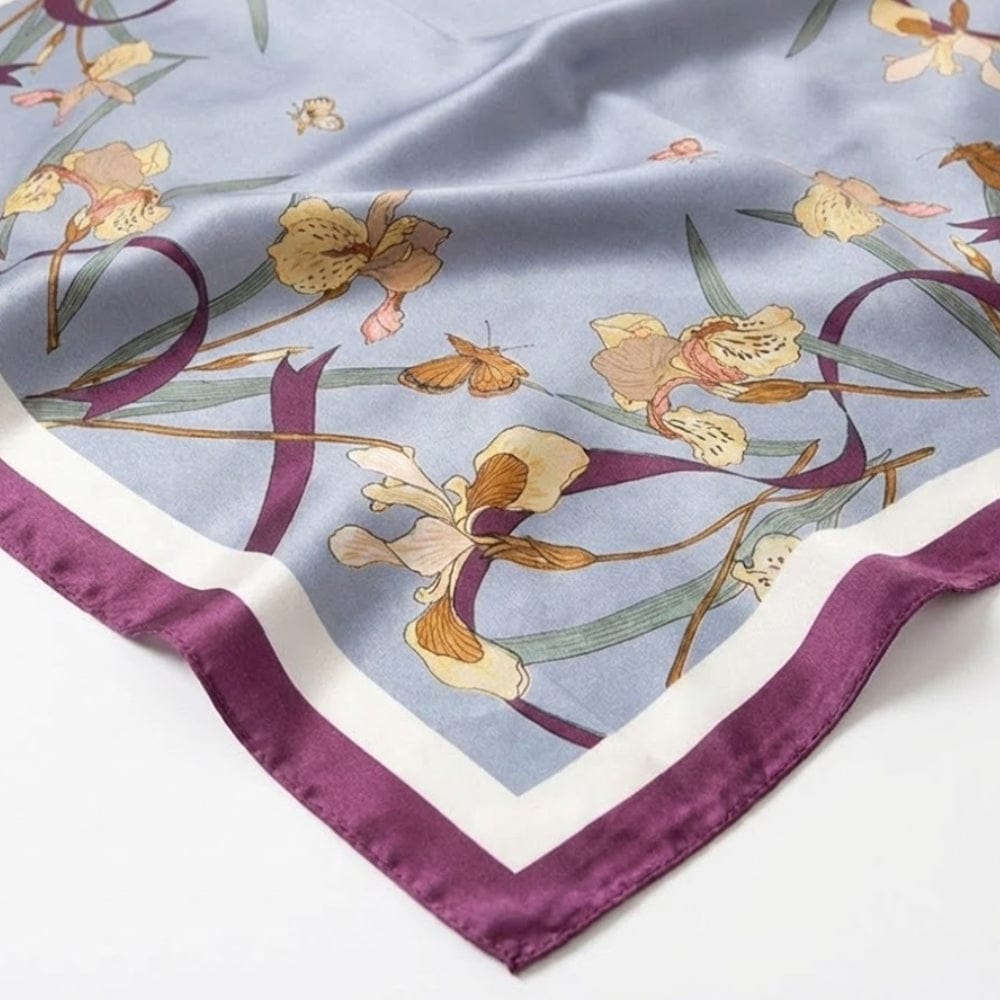 Foulard en satin bleu orné de motifs floraux et bordé d'un liseré violet, posé sur une surface douce