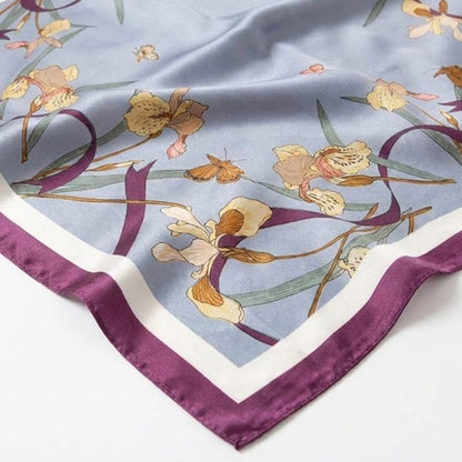 Foulard en satin bleu orné de motifs floraux et bordé d'un liseré violet, posé sur une surface douce