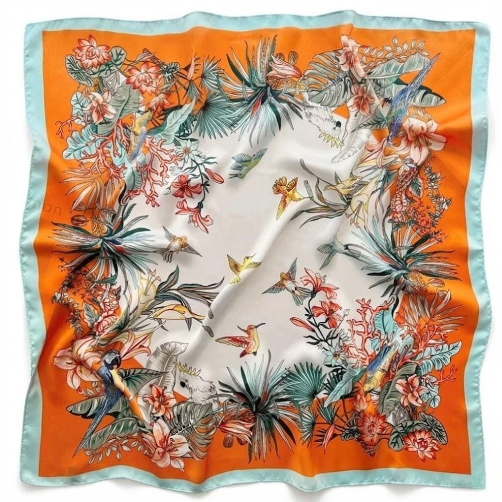 Foulard carré en satin aux motifs floraux colorés sur fond blanc et bordure orange, posé sur une surface plane