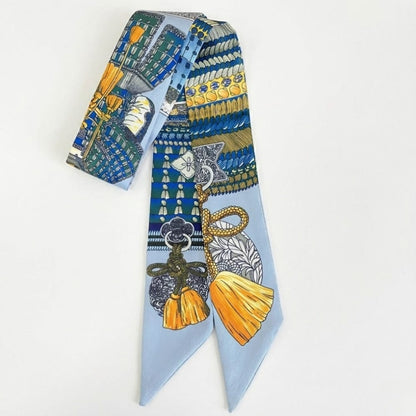 Foulard en soie bleu avec motifs colorés et franges, noué en bandeau sur fond blanc