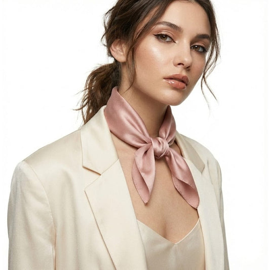 Foulard en soie rose poudré noué autour du cou d'une femme, porté avec une veste beige élégante