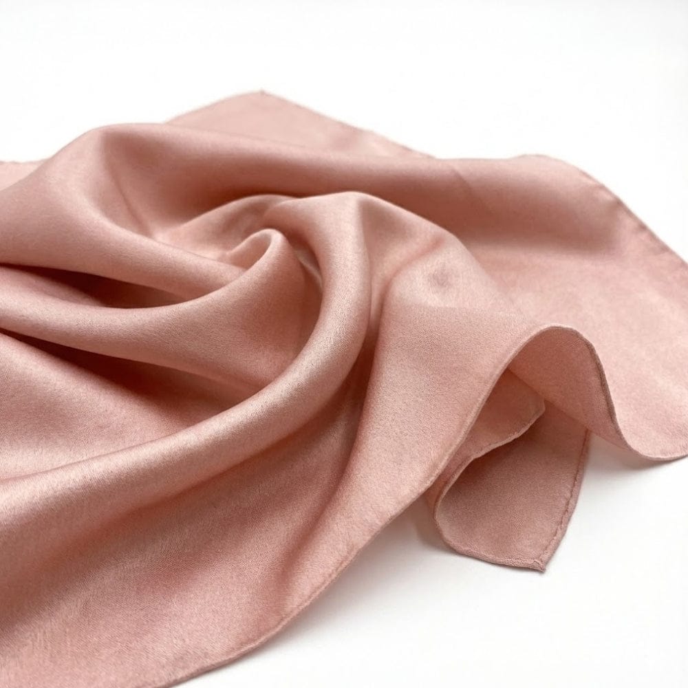Foulard en soie rose poudre, doux et élégant, posé sur une surface blanche, légèrement froissé