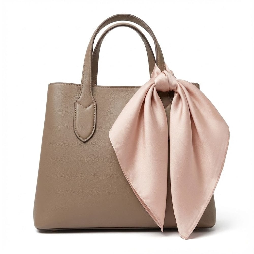 Foulard en soie rose poudré noué sur un sac à main beige, ajoutant une touche d'élégance raffinée