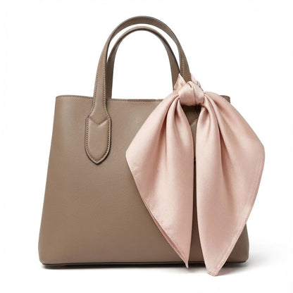 Foulard en soie rose poudré noué sur un sac à main beige, ajoutant une touche d'élégance raffinée