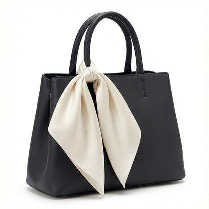 Foulard en satin crème noué sur un sac à main noir, ajoutant une touche élégante et raffinée