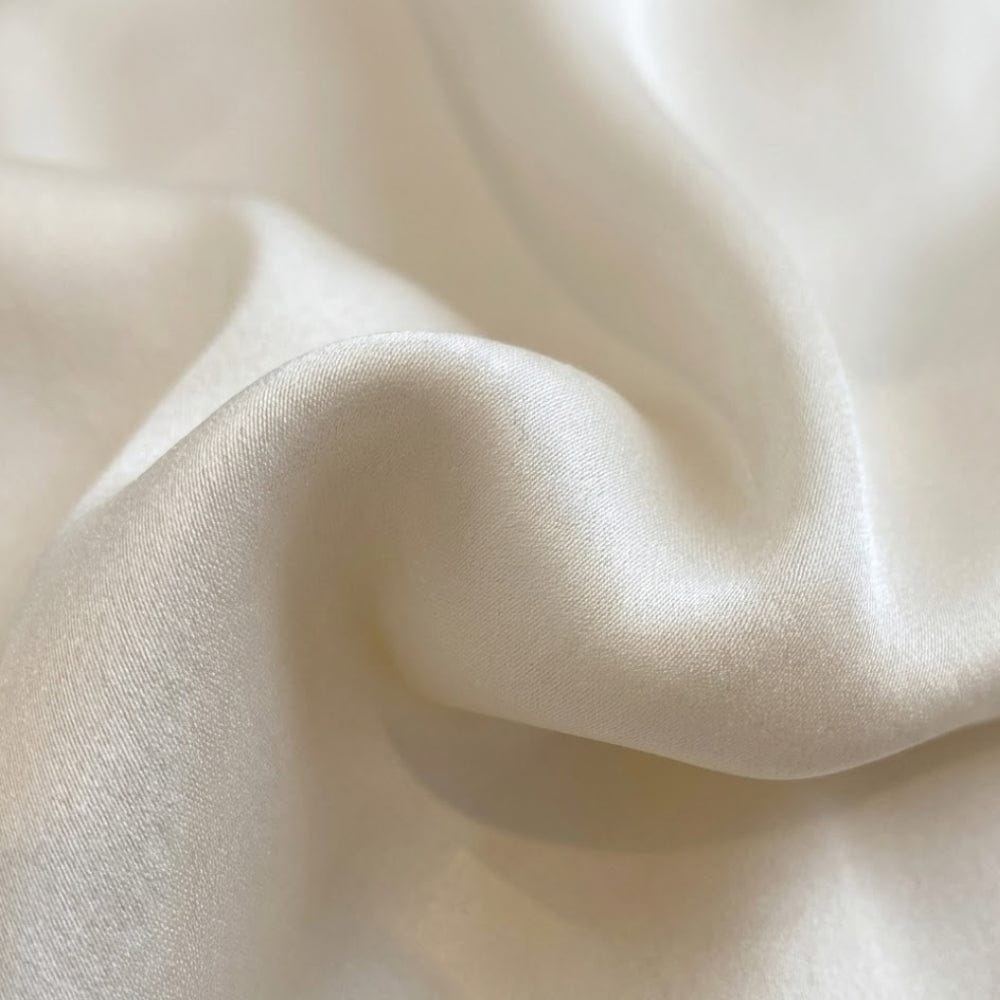 Foulard en soie blanc, doux et brillant, drapé élégamment sur une surface lisse, mettant en valeur sa texture luxueuse