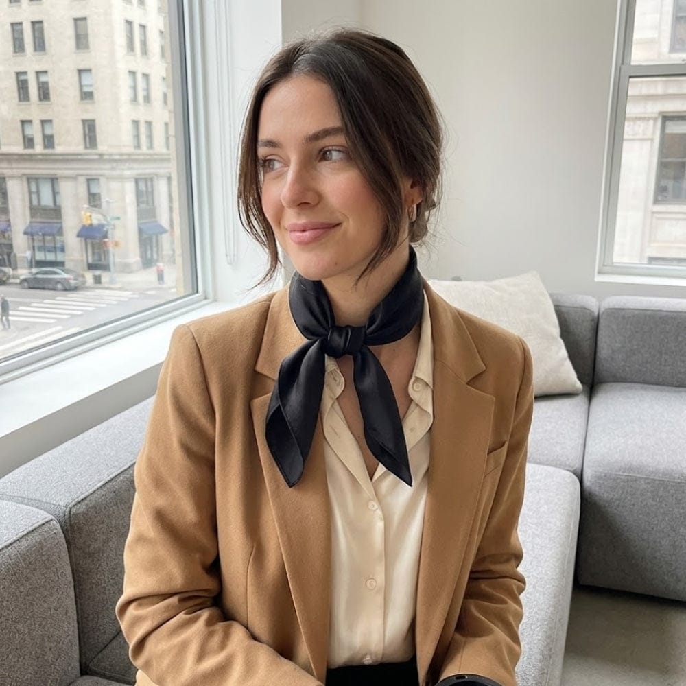 Foulard en soie noir noué autour du cou d'une femme, portant un blazer beige dans un intérieur lumineux