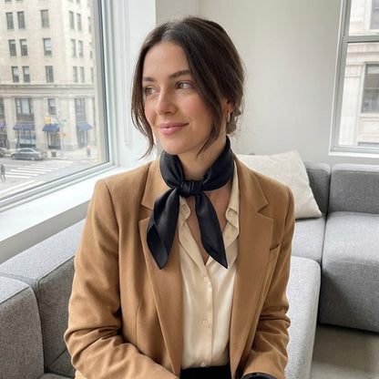 Foulard en soie noir noué autour du cou d'une femme, portant un blazer beige dans un intérieur lumineux