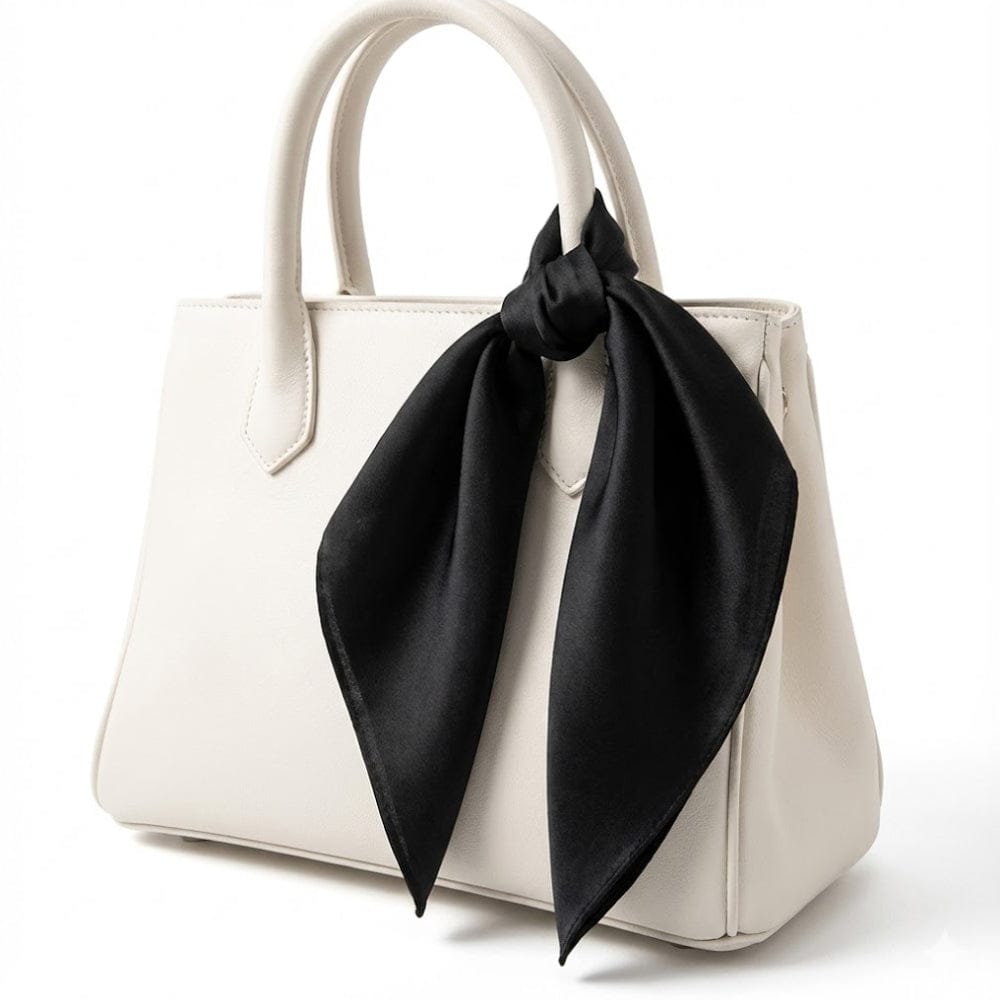 Foulard en soie noir noué sur un sac à main blanc, mettant en valeur sa texture brillante et élégante