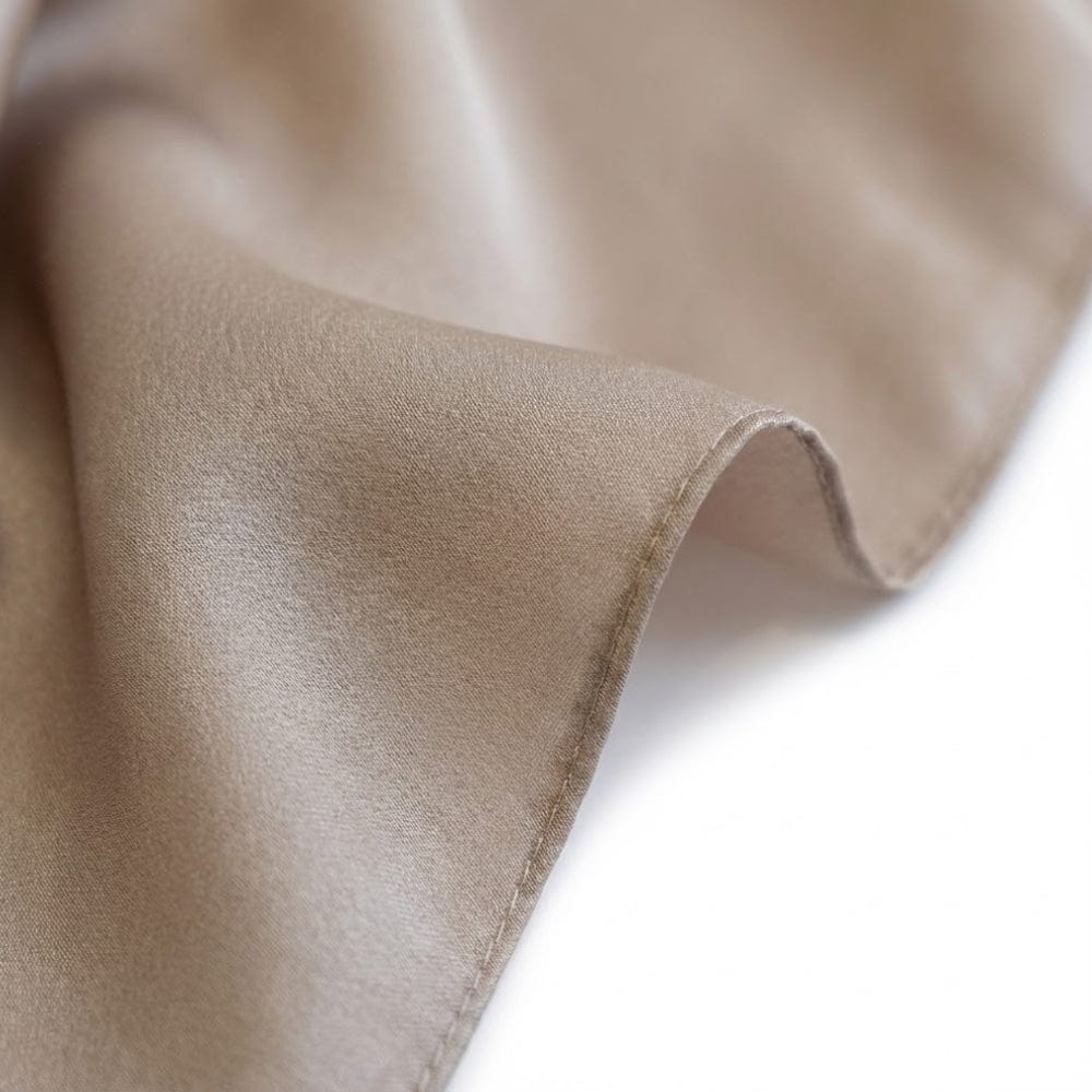 Foulard en soie beige, doux et brillant, drapé élégamment sur un fond blanc