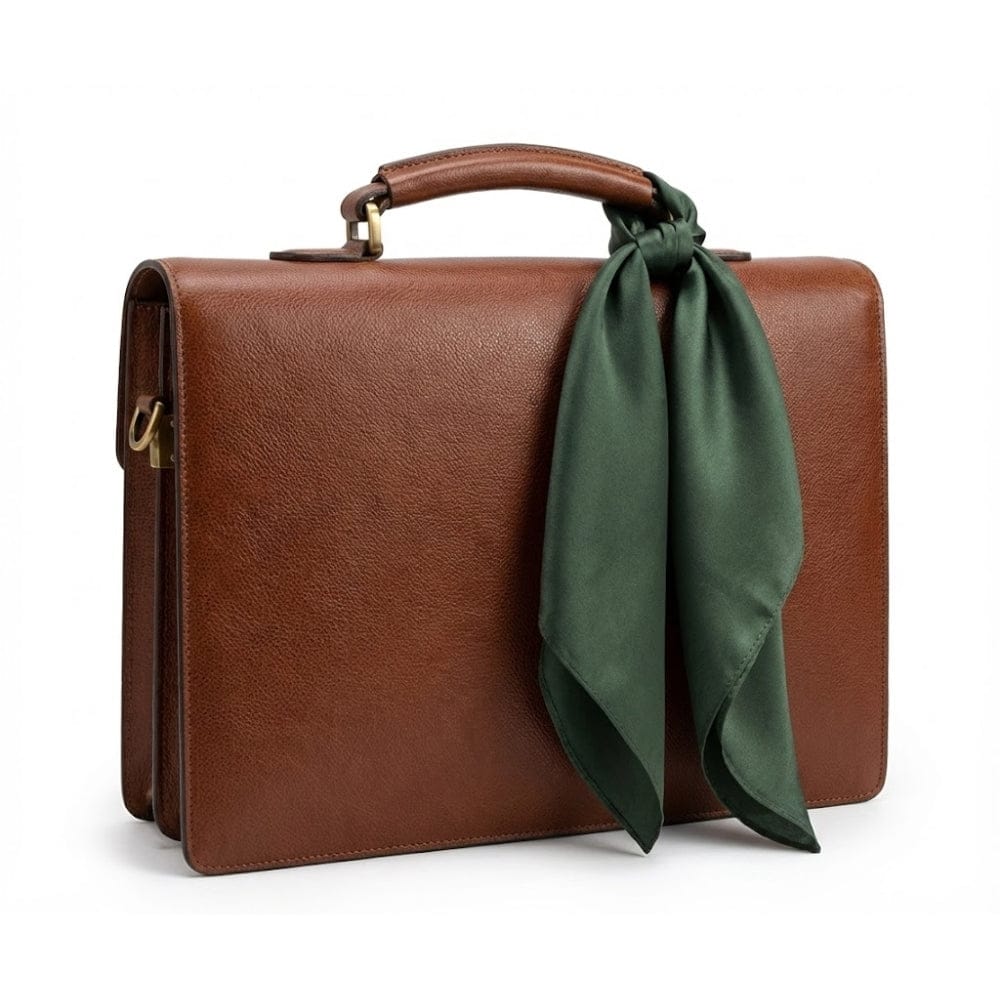 Foulard en soie vert noué élégamment sur une mallette en cuir marron, ajoutant une touche de sophistication